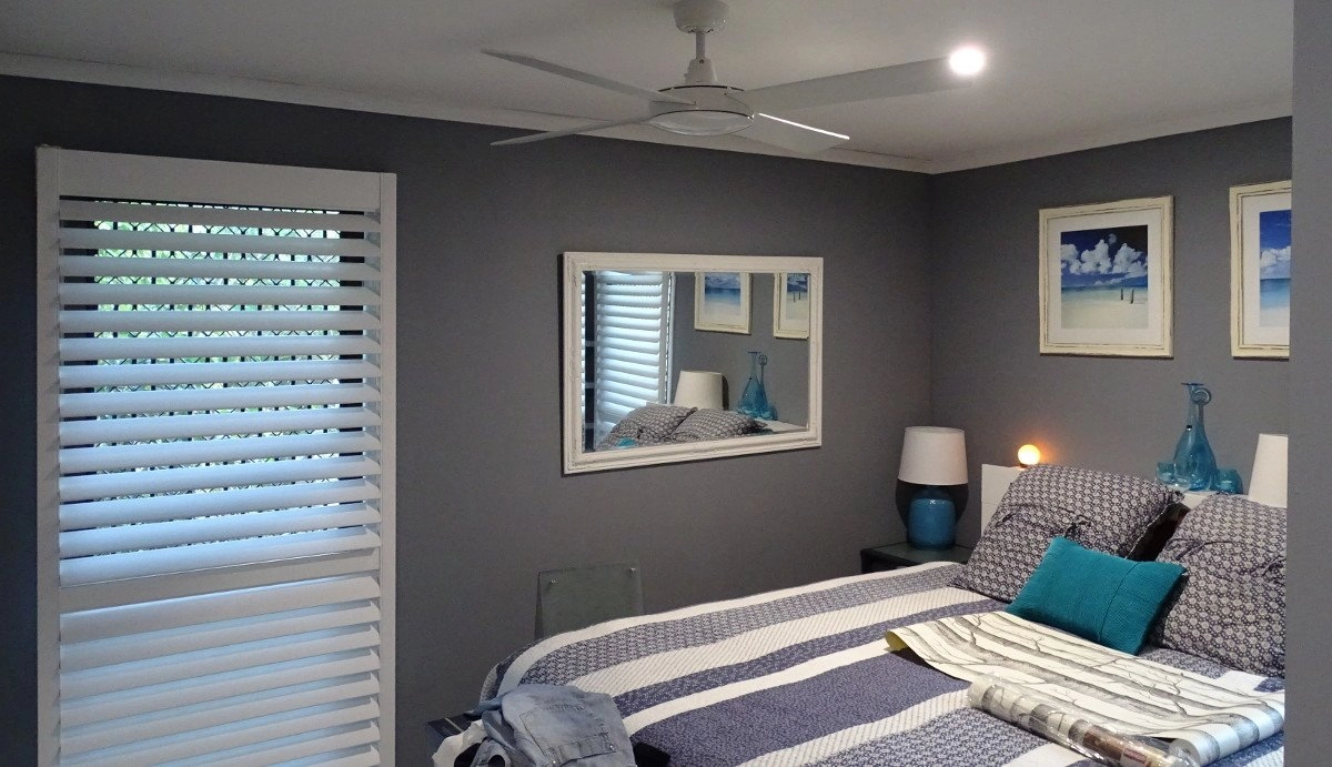 A modern bedroom featuring plantation shutters, a bed with patterned bedding, and decorative wall art.