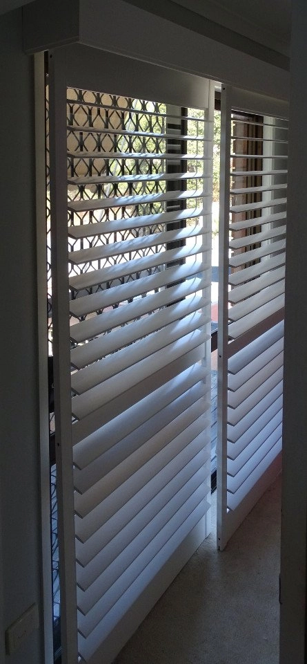 White plantation shutters installed in a doorway, allowing light to filter through the slats.