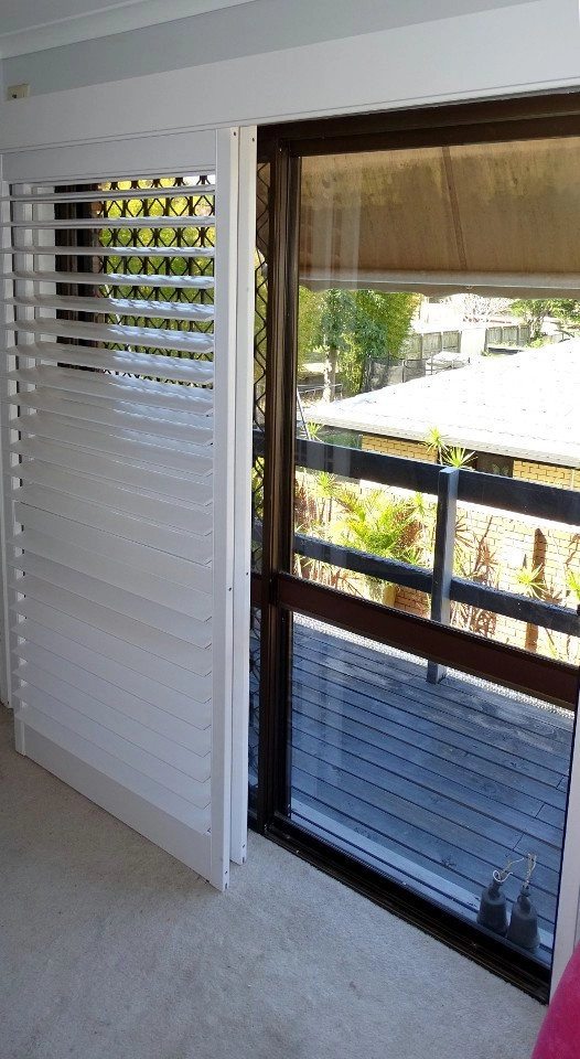 White plantation shutters installed on a window with a view of an outdoor area.